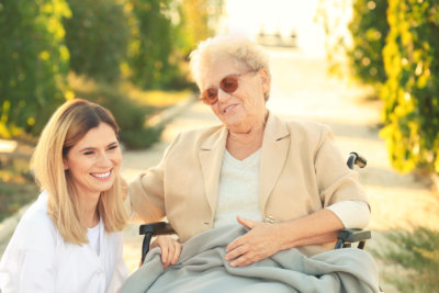 Senior woman in wheelchair and nurse from care home outdoors