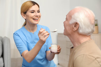 Nurse feeding elderly men with yogurt indoors