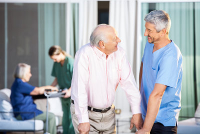 Happy male caretaker looking at disabled senior man at nursing home yard