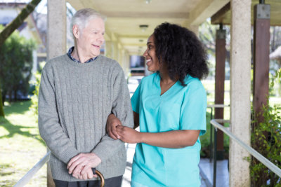 African nurse assisting elderly man outdoor.