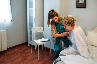 Female caregiver helping elderly female patient to get out of bed